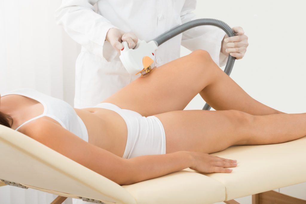 medical professional placing laser hair removal device on female patient’s thigh