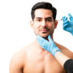 Closeup of doctor's hands injecting botox into the skin of male model on white background