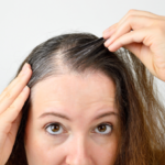 woman is checking white hair while looking at the mirror