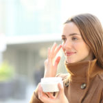 Satisfied woman applying mousturizer cream on her face in winter in the street