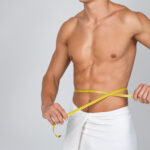 Closeup of unrecognizable sporty muscular man measuring his waist with yellow tape.