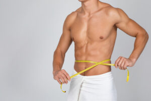 Closeup of unrecognizable sporty muscular man measuring his waist with yellow tape. 